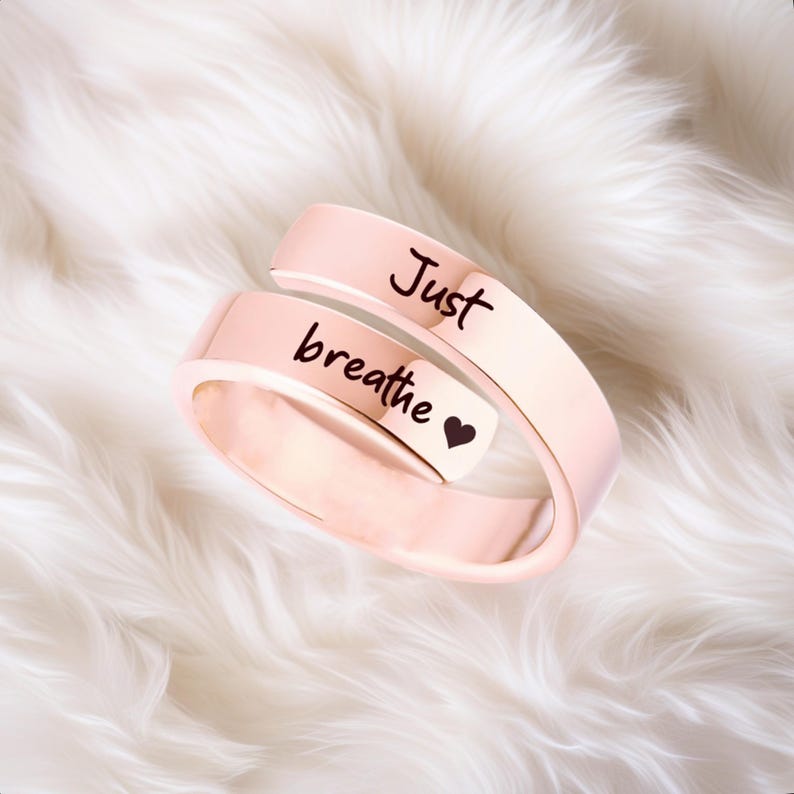 May include: A rose gold-colored ring with the words "Just breathe" and a small heart engraved on it.