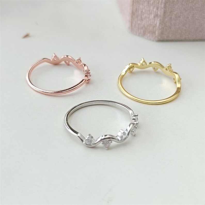 Puede incluir: Tres anillos delicados con un dise&ntilde;o ondulado y peque&ntilde;as piedras transparentes. Los anillos se muestran en plata, oro y oro rosa.