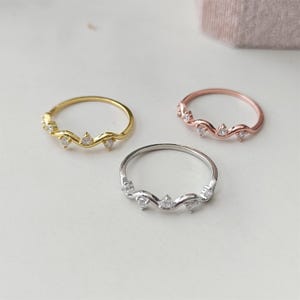 Puede incluir: Tres anillos delicados con un dise&ntilde;o ondulado y peque&ntilde;as piedras transparentes. Los anillos son de oro, oro rosa y plata.