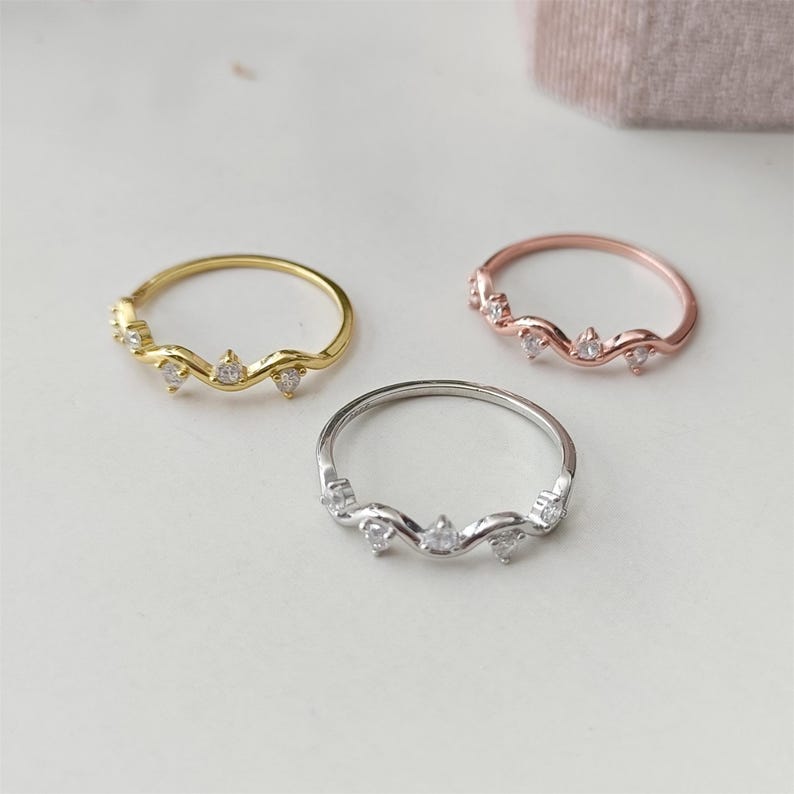 Puede incluir: Tres anillos delicados con un dise&ntilde;o ondulado y peque&ntilde;as piedras transparentes. Los anillos son de oro, oro rosa y plata.