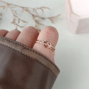 May include: A rose gold ring with a knot design and a row of small clear stones.