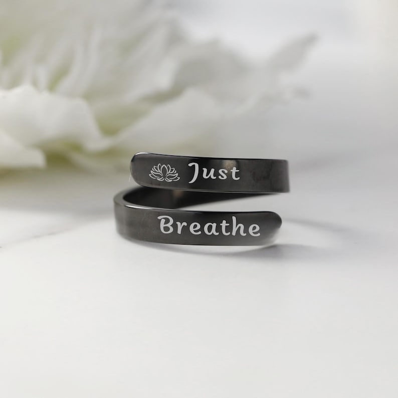 May include: A black metal ring with the words "Just Breathe" and a lotus flower engraved on it.