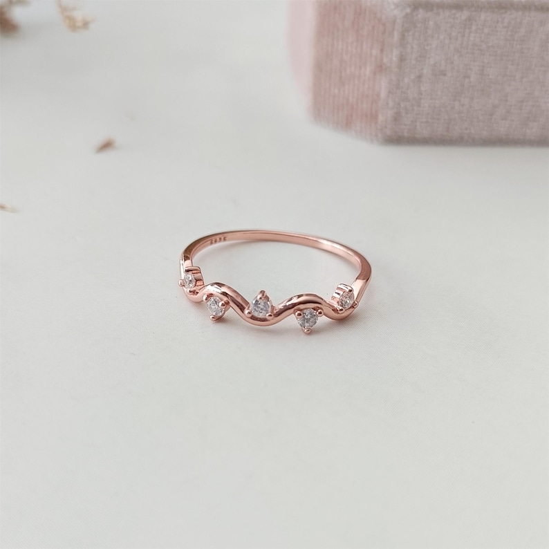 Puede incluir: Un delicado anillo de oro rosa con una banda ondulada y cinco peque&ntilde;as piedras transparentes.