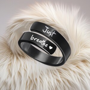 May include: Black ring with the words "Just breathe" and a small heart engraved on it.