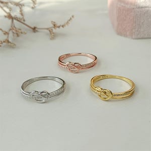 May include: Three knot rings with a row of small clear stones. The rings are silver, rose gold, and gold.