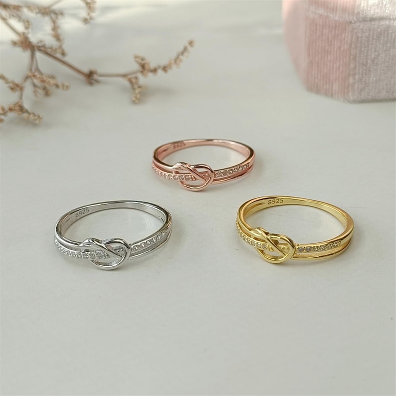 May include: Three knot rings with a row of small clear stones. The rings are silver, rose gold, and gold.
