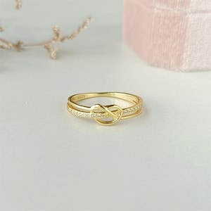 May include: A gold ring with a knot design and small clear stones. The ring is marked with the number "5925".