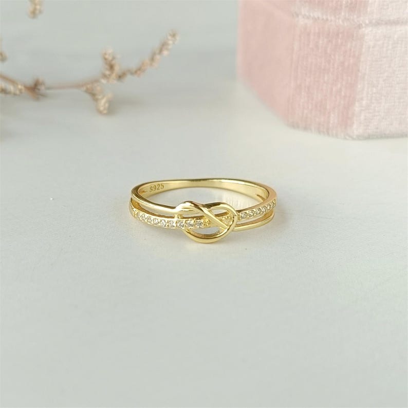 May include: A gold ring with a knot design and small clear stones. The ring is marked with the number "5925".
