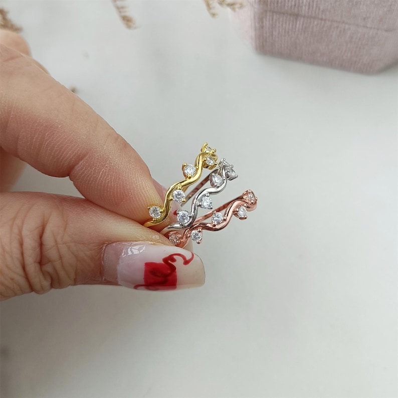 Puede incluir: Tres anillos delicados con un dise&ntilde;o ondulado y peque&ntilde;as piedras transparentes. Los anillos son de oro, plata y oro rosa.