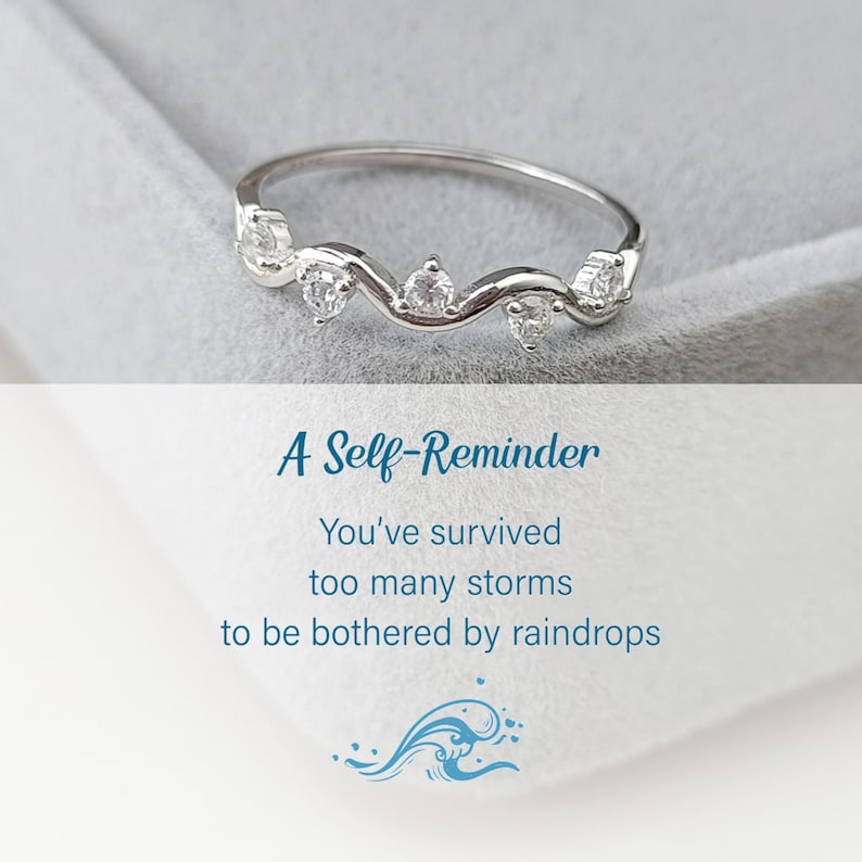 Puede incluir: Un anillo de plata con una banda ondulada y peque&ntilde;as piedras transparentes. El anillo est&aacute; en una caja blanca con el texto "A Self-Reminder You've survived too many storms to be bothered by raindrops" y un gr&aacute;fico de una ola azul.