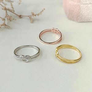 May include: Three rings with a knot design. The rings are silver, gold, and rose gold.