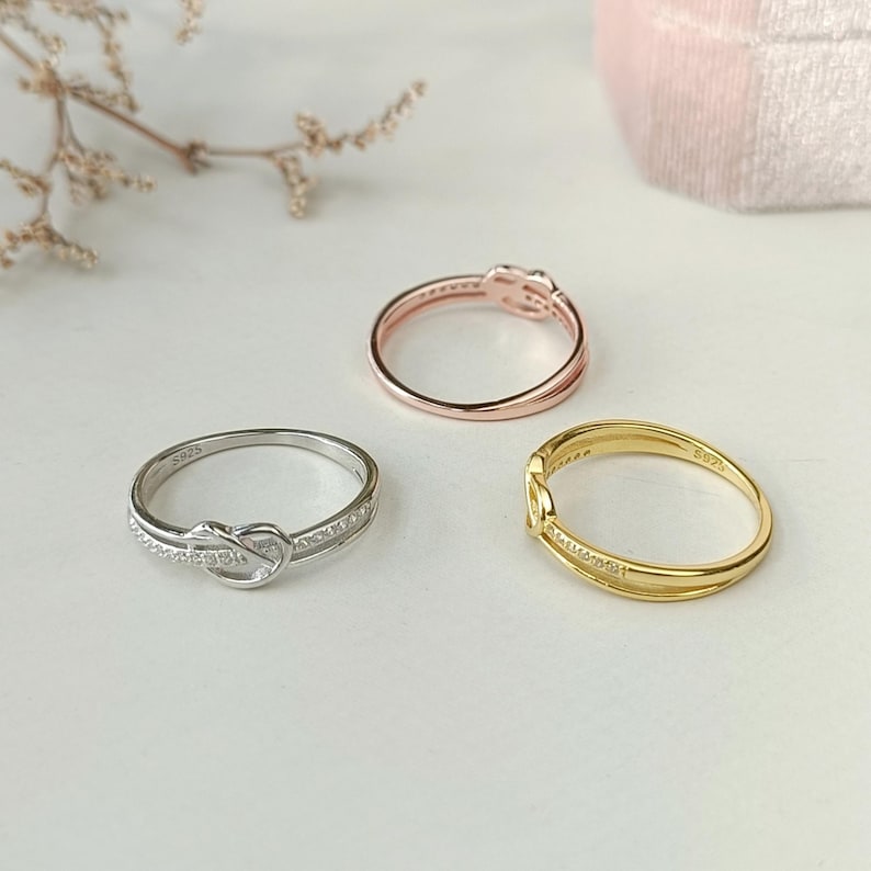 May include: Three rings with a knot design. The rings are silver, gold, and rose gold.