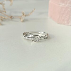 May include: A silver ring with a knot design and a row of small clear stones.