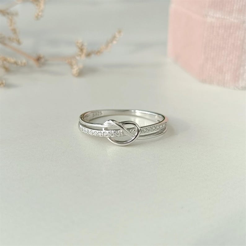 May include: A silver ring with a knot design and a row of small clear stones.