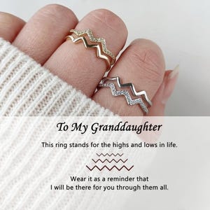 May include: Two zig-zag rings with clear stones. The rings are stacked on a finger. The text "To My Granddaughter" is below the rings. The text "This ring stands for the highs and lows in life." is below the text "To My Granddaughter". The text "Wear it as a reminder that I will be there for you through them all." is below the text "This ring stands for the highs and lows in life."