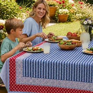 May include: A rectangular tablecloth featuring a blue and white striped pattern with a wide red border decorated with white floral motifs. The fabric displays a geometric design along the edges and a repeating vertical stripe pattern across the center.