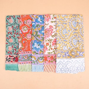 May include: A collection of colorful, floral-patterned textiles. The designs include various flowers and foliage in shades of teal, orange, purple, pink, and yellow. Each textile has a patterned border. The textiles are arranged side by side.