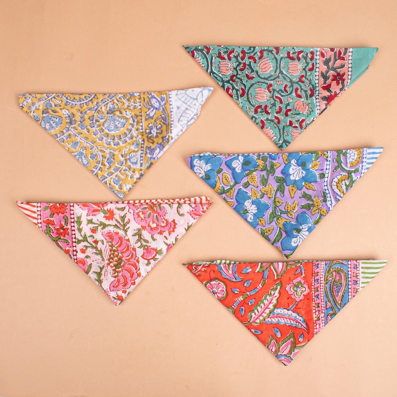 May include: A collection of five colorful, triangular bandanas with floral and paisley patterns. The bandanas feature a variety of colors, including yellow, blue, pink, red, and green. Each bandana has a unique design, making them a vibrant and stylish accessory.