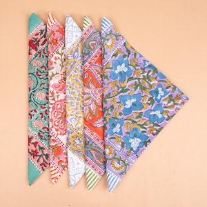 May include: Five colorful bandanas with floral patterns. The bandanas are arranged in a fan shape, showcasing a variety of designs. Colors include teal, pink, yellow, orange, and purple, each with unique floral and paisley motifs. The edges are finished with striped borders.