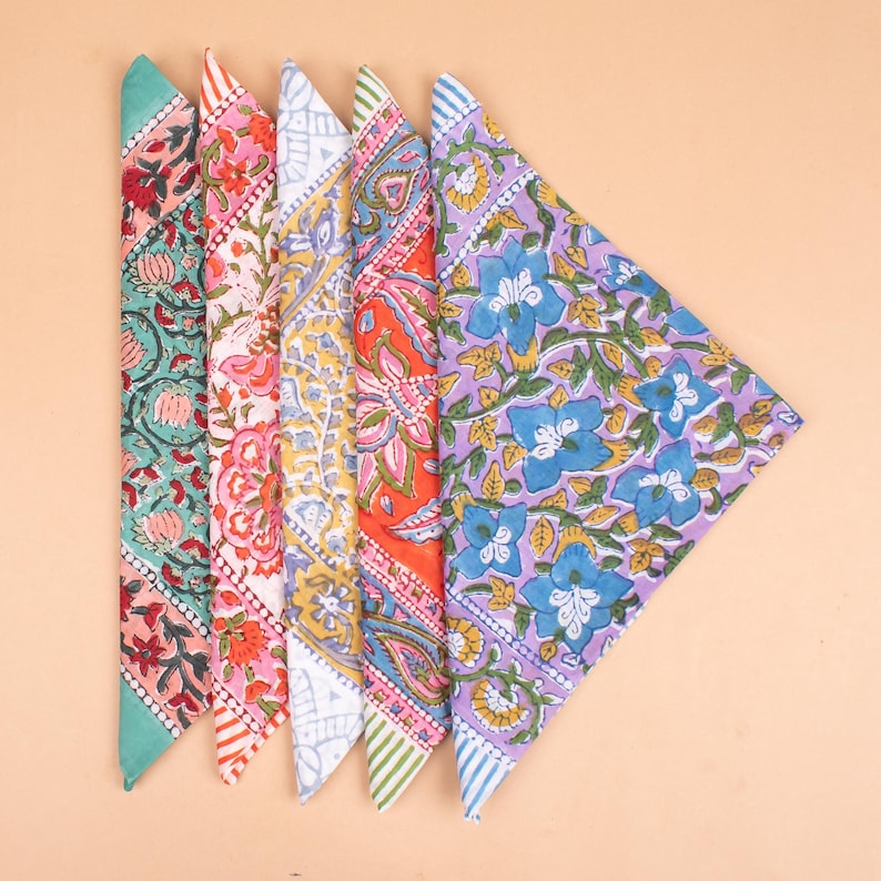 May include: Five colorful bandanas with floral patterns. The bandanas are arranged in a fan shape, showcasing a variety of designs. Colors include teal, pink, yellow, orange, and purple, each with unique floral and paisley motifs. The edges are finished with striped borders.
