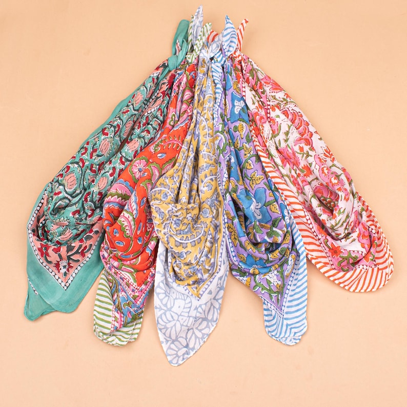 May include: A collection of colorful, patterned scarves. The scarves feature floral and paisley designs in shades of green, red, yellow, blue, and pink. Each scarf is folded and arranged in a fan shape, showcasing the variety of patterns and colors.