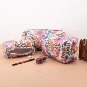 May include: Three floral patterned zippered pouches in different sizes. The pouches are made of white fabric with pink, orange, and green floral designs. The pouches are lined with white fabric and have a zipper closure.