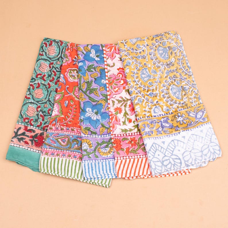 May include: A collection of colorful, patterned fabric cloths. Each cloth features a unique floral design in shades of green, orange, purple, pink, and yellow. The edges are finished with striped borders.