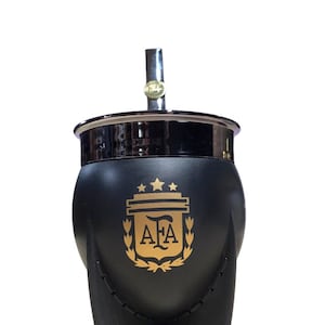 Puede incluir: Mate negro y dorado con tapa plateada y bombilla. El mate tiene un diseño de escudo con las letras "AFA" en su interior y tres estrellas arriba.