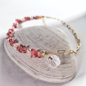 Op de afbeelding: Een gouden ketting met een roze en witte schelpbedel. De ketting is gemaakt met kleine roze en witte stenen en een parel.