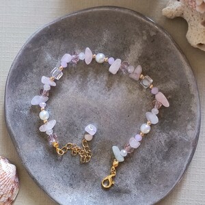 May include: A delicate bracelet made with pink and white stones, pearls, and gold accents. The bracelet has a lobster clasp closure.