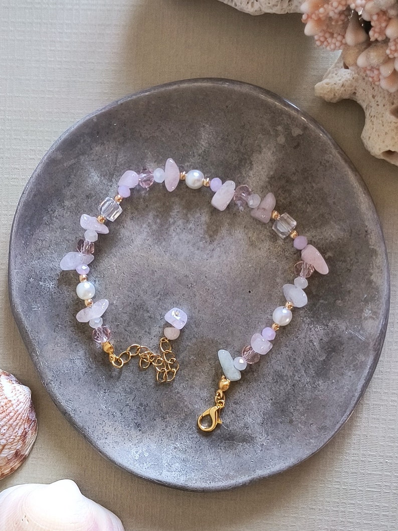 May include: A delicate bracelet made with pink and white stones, pearls, and gold accents. The bracelet has a lobster clasp closure.