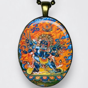 May include: Oval pendant necklace with a detailed illustration of a deity in blue, orange, and yellow. The pendant hangs from a dark chain. The artwork features multiple arms and intricate details, set against a vibrant background.