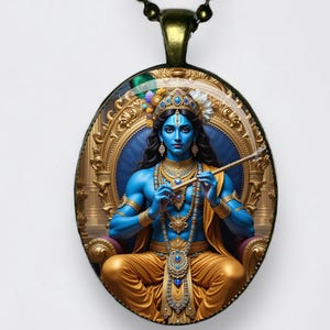 Puede incluir: Un colgante ovalado que muestra una figura de piel azul con cabello largo y oscuro, con joyas doradas y prendas amarillas, tocando una flauta mientras está sentada en un trono dorado ornamentado. El colgante cuelga de una cadena de bolas oscura.