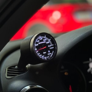 Può includere: Un manometro di sovralimentazione turbo nero e bianco con un ago bianco che punta a 1,5 bar. Il manometro è etichettato "Turbo" e ha un indicatore "Peak" e "Diameter". Il manometro è montato sul cruscotto di un'auto.