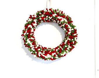 May include: A Christmas wreath with a loop design, featuring red, green, and white fabric. The wreath has a textured appearance and is suspended against a white backdrop. Ideal for festive home decoration during the holiday season.