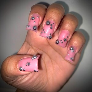May include: Pink press-on nails with silver 3D embellishments. The nails are square shaped and have a glossy finish.