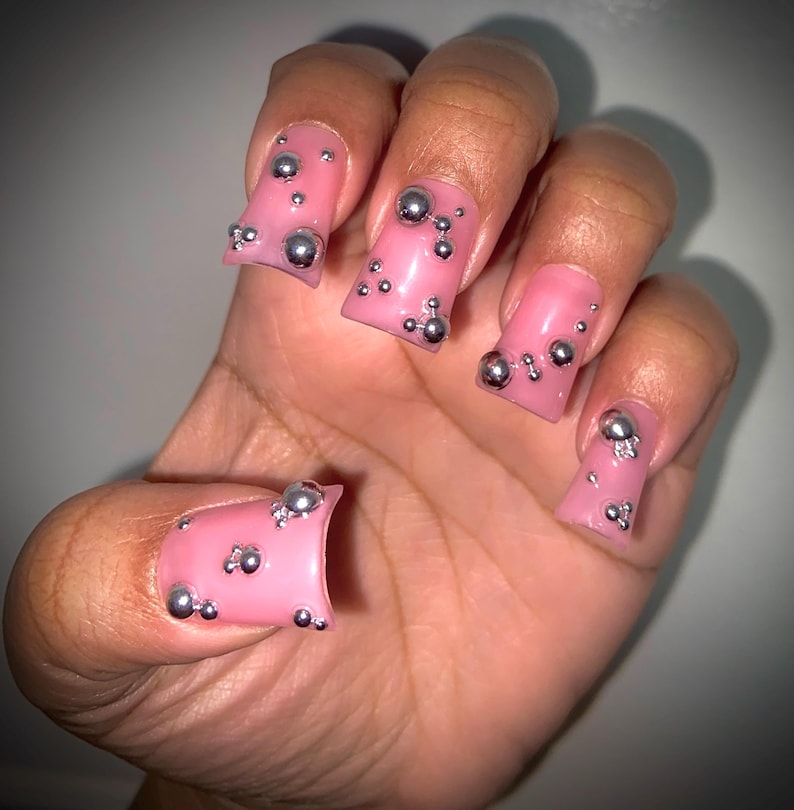 May include: Pink press-on nails with silver 3D embellishments. The nails are square shaped and have a glossy finish.