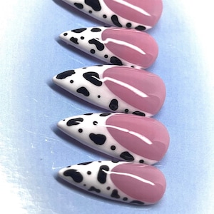 May include: Five long, pointed, false nails with a cow print design on the bottom half and a pink color on the top half.