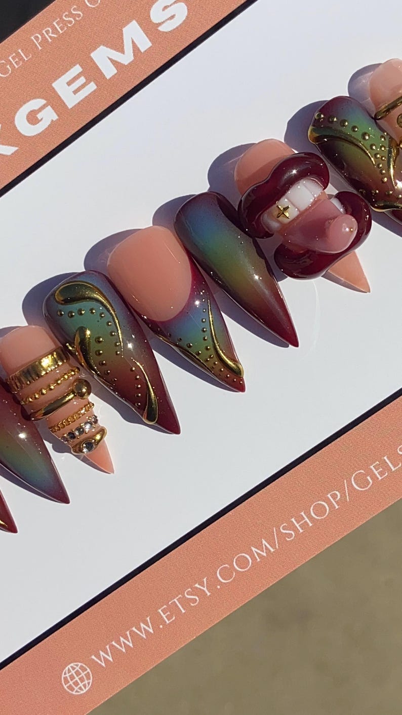 May include: A set of custom press-on nails with a variety of designs. Some nails feature a gradient of colors, gold embellishments, and a 3D lip design. The nails are displayed on a white surface with text that reads "GEMS" and "www.etsy.com/shop/gels".