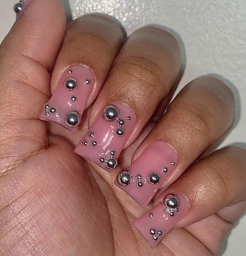 May include: Pink square-shaped press-on nails with silver 3D bubble embellishments.