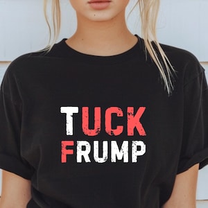 May include: Black t-shirt with white text that reads "TUCK FRUMP" in a distressed font. The text is in red and white.