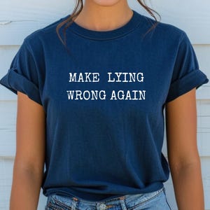 May include: A navy blue t-shirt with the text "MAKE LYING WRONG AGAIN" printed in white.