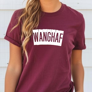Puede incluir: Una camiseta granate con la palabra "WANGHAF" impresa en letras blancas dentro de un rectángulo blanco. La camiseta tiene mangas cortas y cuello redondo.