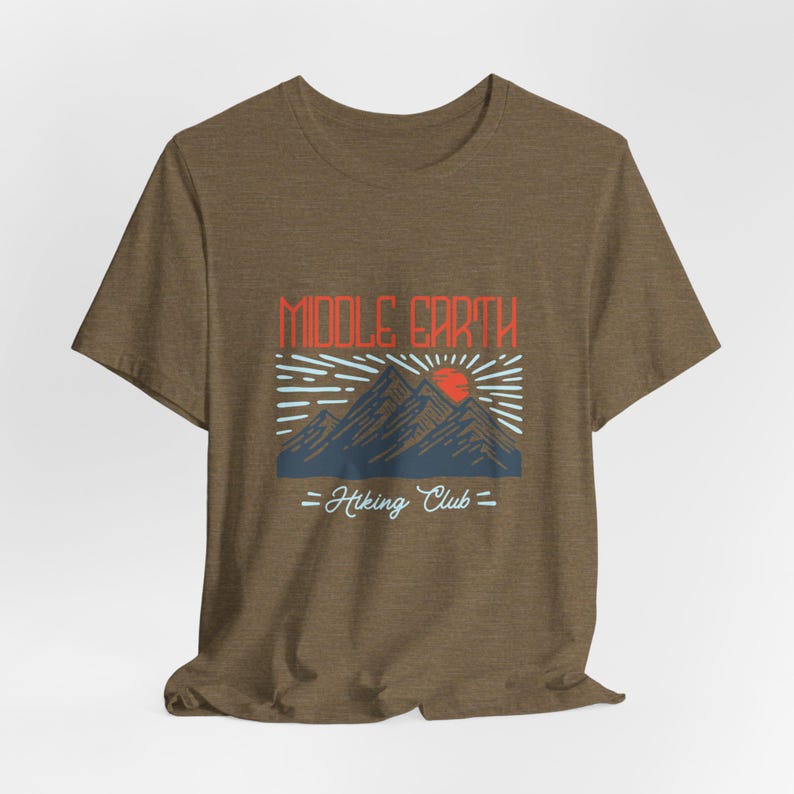 Op de afbeelding: Een bruin t-shirt met een grafisch ontwerp van bergen en een zon met de tekst "Middle Earth Hiking Club".
