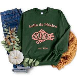 May include: A dark green sweatshirt with the text "Golfo de M&eacute;xico est. 1550" and a pink stylized fish graphic.