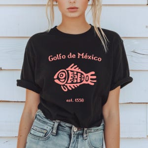 May include: Black t-shirt with a pink fish graphic and the text "Golfo de M&eacute;xico est. 1550".
