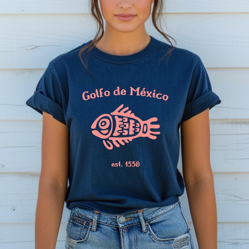 May include: A navy blue t-shirt with a pink fish graphic and the text "Golfo de M&eacute;xico est. 1550".