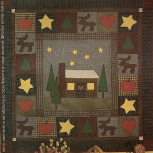 May include: A brown, green, and red patchwork quilt with a cabin, trees, stars, moose, and apples. The quilt is made of squares and rectangles.