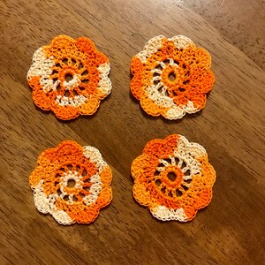May include: Four crocheted doilies in orange and white. The doilies are circular and have a spiral pattern in the center.