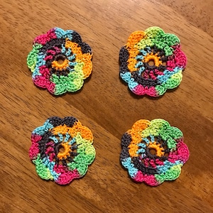 May include: Four circular crochet appliques arranged in a square formation. Each piece features a vibrant, multi-colored yarn pattern with shades of pink, orange, yellow, light blue, lime green, and dark navy blue, forming a swirling floral design.